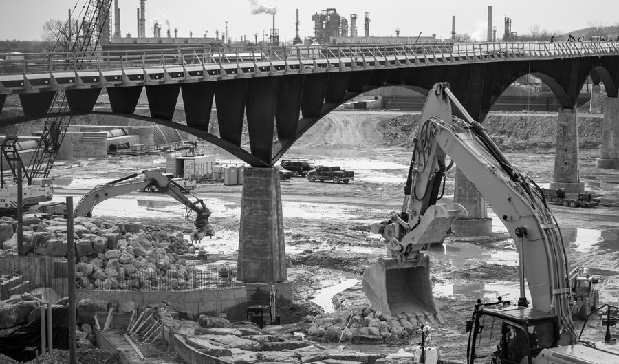 Bridge under construction over a river crossing, with excavators working on the pier foundations below