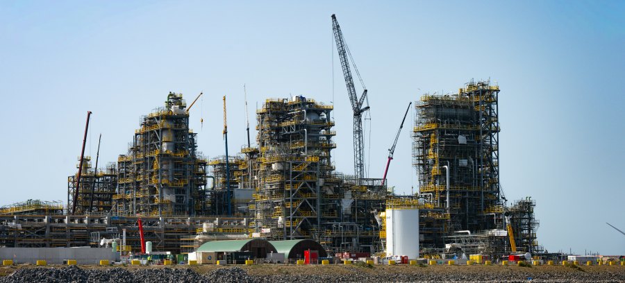 Large industrial process facility under construction, with steel structures, scaffolding and multiple cranes across the site