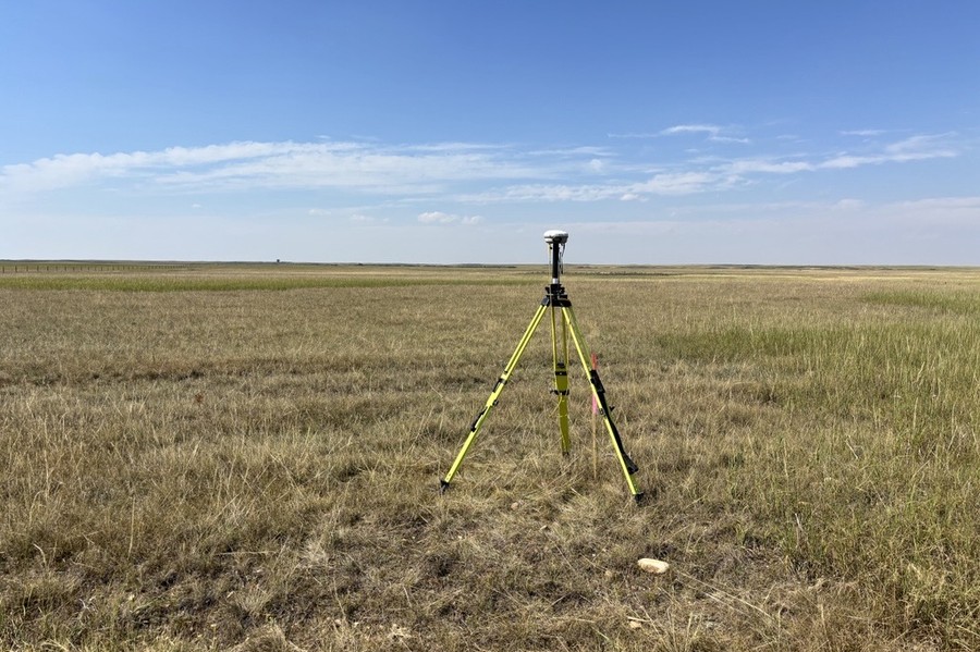 Survey-grade GNSS receiver on a tripod over a control point on open prairie
